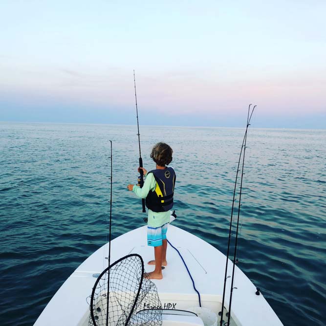 Boy holding fishing rod standing at the  bow facing the ocean at sunset in Florida Keys